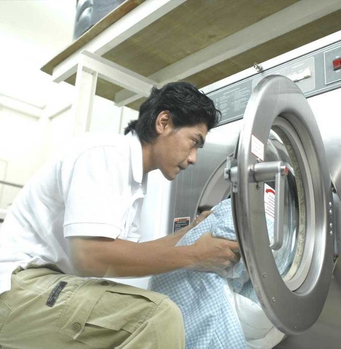 pencucian basah kakitangan sedang memasukkan pakaian ke dalam mesin basuh