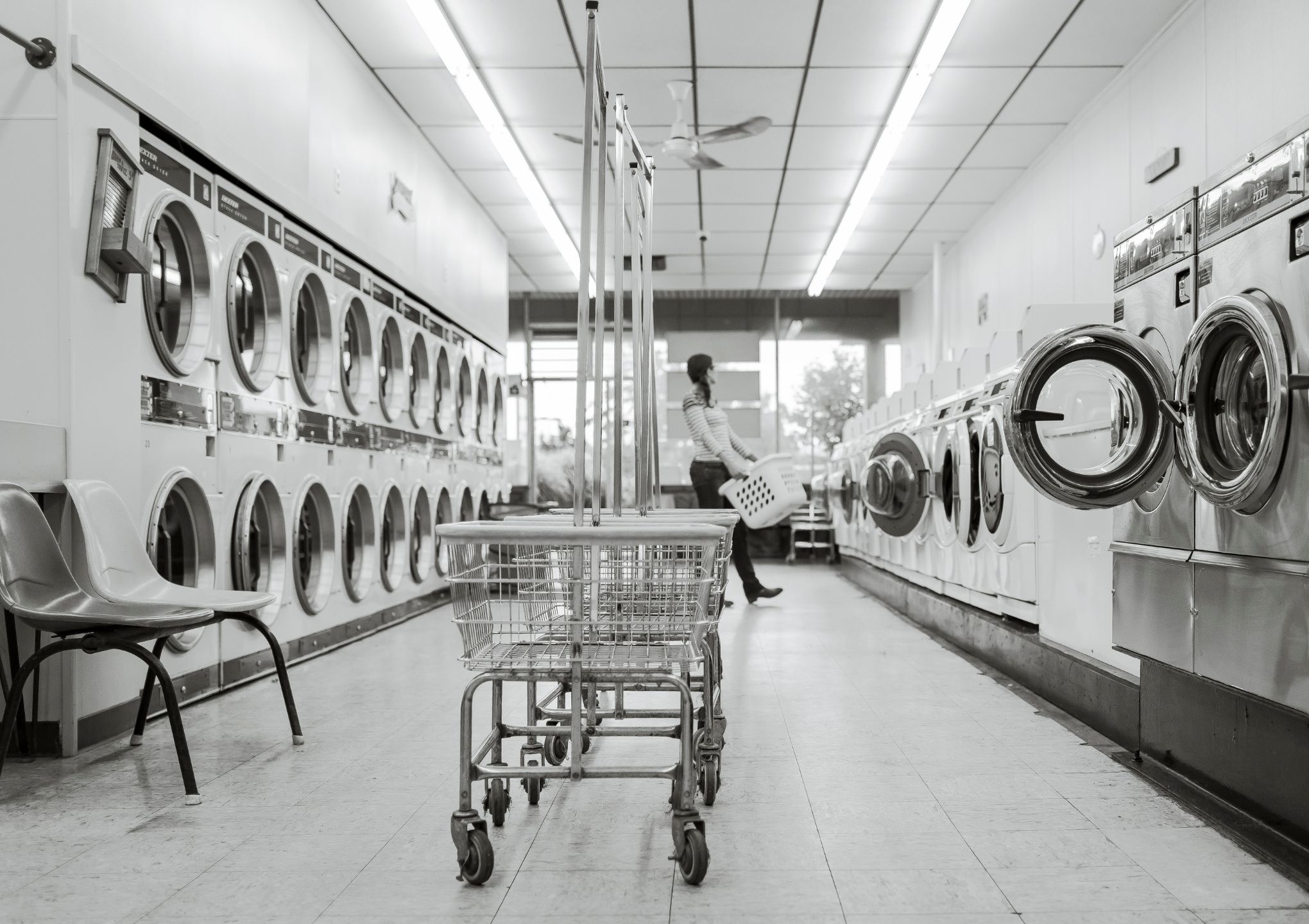 a woman is carrying a laundry basket inside the coin laundry shop - Post Featured Image